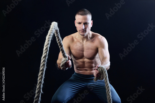 Fotografie, Obraz Young muscular man dynamically workout with battle rope