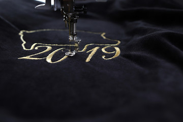 Wall Mural - Detail of embroidery machine stitching 2019 chinese new year motive with precious gold yarn on black velvet - tilted view with blurred surrounding as copy space for text