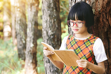 Wall Mural - Cute little girl with glasses reading book in the pine forest