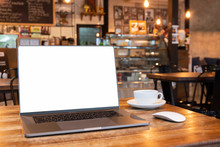 Blank screen laptop with mouse and coffee cup on wooden table in coffe shop.