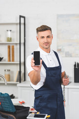 Wall Mural - smiling adult handyman holding pipe and smartphone with blank screen