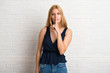 © luismolinero - Blonde woman showing a sign of closing mouth and silence gesture putting finger in mouth on white brick wall background
