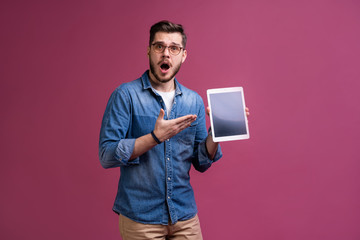 Wall Mural - Happy attractive young man standing and using tablet over pink background.