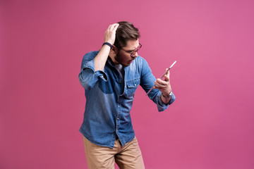 Wall Mural - Happy attractive young man standing and using tablet over pink background.