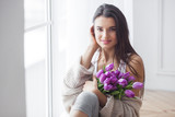Fototapeta Tulipany - Young attractive woman with bouquet of flowers. Beautiful girl at home with pink tulips. Female in the bedroom.