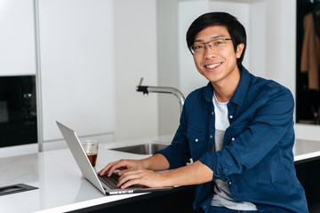 Wall Mural - Smiling asian man working on laptop computer