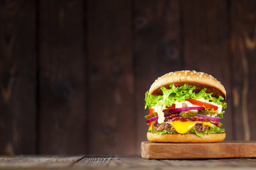 Delicious burger with bacon, cucumbers, lettuce, cheese, onion and tomatoes on dark wooden background