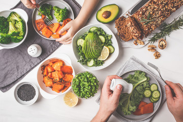 Healthy vegan food lunch, top view. Vegetarian dinner table, people eat healthy food. Salad, sweet potato, vegan cake, vegetables on white background.