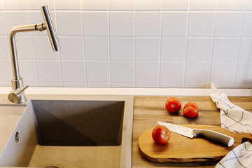 Wall Mural - Cooking food on modern kitchen, knife on wooden cutting board with vegetables, spices on wooden tabletop at sink with water. Home food. Stylish kitchen furniture in grey color