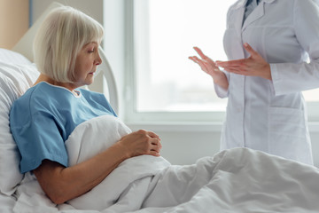 Wall Mural - female doctor consulting sad senior woman with grey hair lying in hospital bed