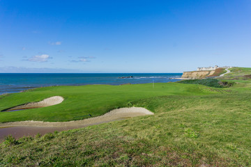 Wall Mural - Golf course putting green on the cliffs by the pacific ocean, Resort in the background, Half Moon Bay, California