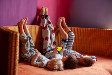 Funny kids lay on sofa to play computer games on smartphone. Parents gave the children a new phone for Christmas. Modern children are well aware of latest technology. Brothers are happy together