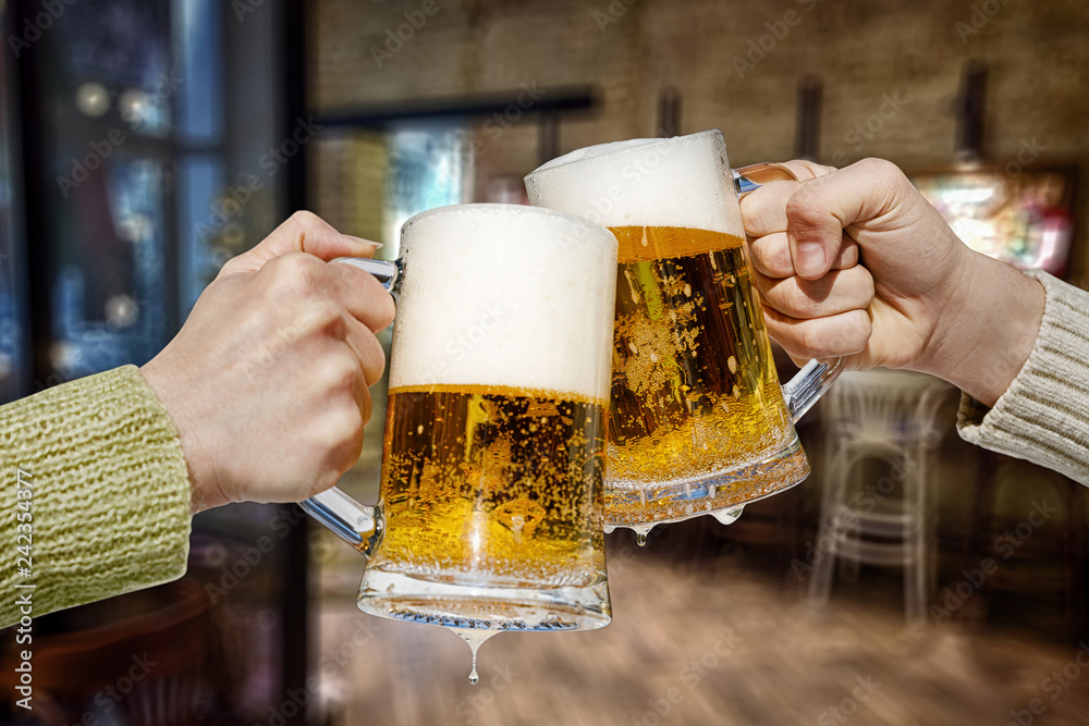 Two hands are clinking beer mugs. Stock Photo | Adobe Stock