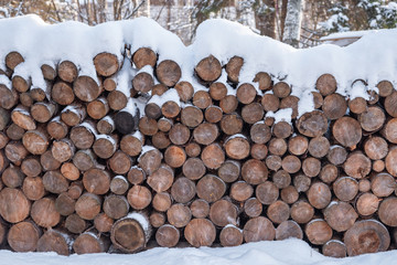 Firewood stacked in piles, covered with snow. cutted trunks in a alpine hut in winter forest