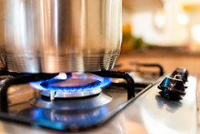 Macro Closeup Of Modern Luxury Gas Stove Top With Blue Fire Flame Knobs And Stainless Steel Pot With Reflection And Bokeh Blurry Blurred Background
