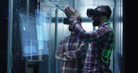 Medium shot of two male technician in VR glasses using a virtual interface while working in a data center