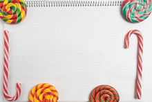 Back To School Background. Colorful Sweet Candys On Blank Notepad With Spiral. Striped Candy Canes And Spiral Lollipops On Paper Exercise Book In A Cell