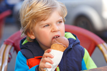 Wall Mural - Cute adorable kid boy eating ice cream in outdoor cafe. Happy child on sunny day. Healthy toddler with sweet dessert in gelateria restaurant