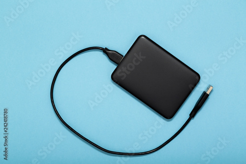 Fotografia Black external hard disk with USB cable on blue background