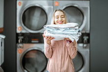 Young Woman Enjoying Clean Ironed Clothes In The Self Serviced Laundry With Dryer Machines On The Background