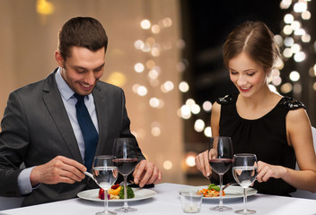 Sticker - people and leisure concept - smiling couple eating main course with red wine at restaurant over festive lights on background