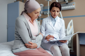 Wall Mural - worried female doctor holding diagnosis and consulting upset senior woman with cancer in hospital