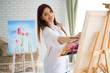 Сute girl artist paints on canvas painting on the easel. Model in the studio