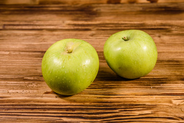 Two ripe green apples on a wooden table