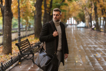 Wall Mural - Photo of adult stylish man 30s wearing warm clothes walking outdoor through autumn park, and looking aside