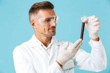 Poster - Portrait of medical doctor wearing white uniform holding test tubes with blood, standing isolated over blue background