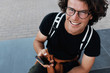© iuricazac - Top view of Caucasian happy man sitting outdoors texting messsages on mobile phone. Young male with curly hair wears spectacles resting in the city using free wireless on smart phone.