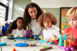© Monkey Business - Female teacher sitting at table in play room with three kindergartne children constructing, selective focus