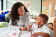 © Monkey Business - Female infant school teacher working one on one with a young schoolboy, sitting at a table smiling at each other, close up