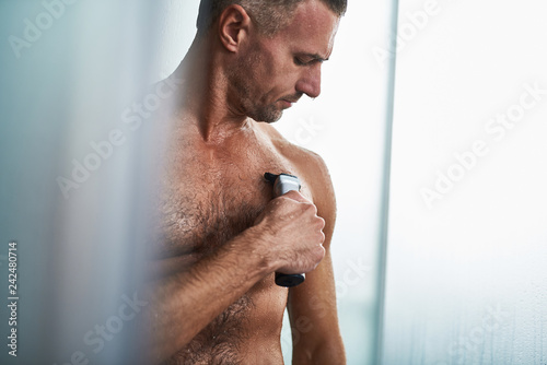 Handsome Young Man Using Electric Razor To Remove Hair From Chest