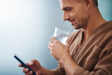Handsome young man with cool drink using cellphone on blue background
