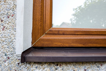 Close-up detail of white plastered house wall with newly installed new brown plastic window and metal windowsill. Modern technology, warm and comfortable home, professional job concept.