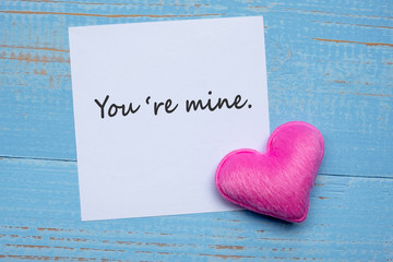 YOU'RE MINE word on paper note with pink heart shape decoration on blue wooden table background. Love, Wedding, Romantic and Happy Valentine’ s day holiday concept