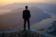  back of a young man in costume standing on a mountain at sunset. The groom or businessman looks from the top.