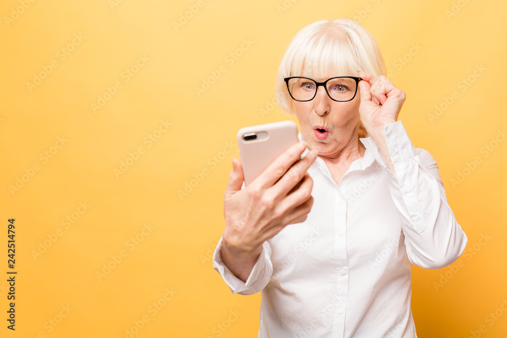 Wow! Phone conversation. Surprised aged woman using phone, isolated over yellow background. - obrazy, fototapety, plakaty 