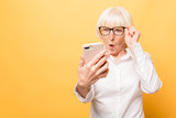 Fototapeta  - Wow! Phone conversation. Surprised aged woman using phone, isolated over yellow background.