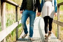 Young Expecting Couple, Dressed In Modern Casual Way, Walking On Wooden Pier During Sunny Day In The Woods, Immersed In Nature