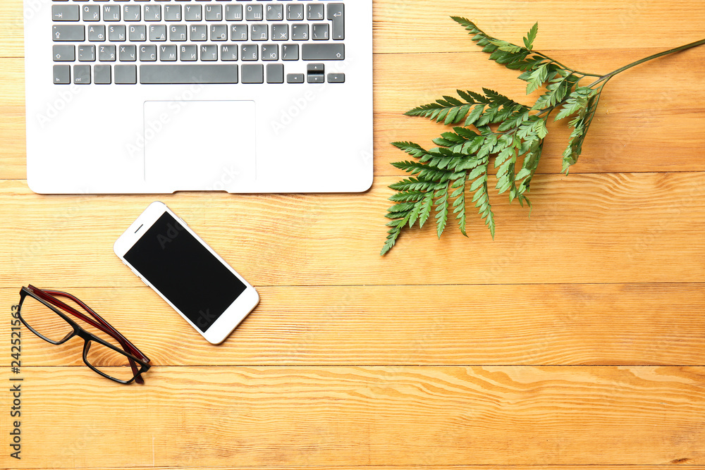Laptop, phone, glasses and tropical leaf on wooden table