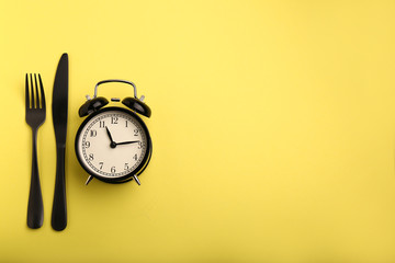 Alarm clock and cutlery on color background. Diet concept