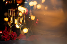 Glasses Of Champagne On The Background Of Lights With Roses And Red Ribbon