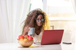© Paul - Beautiful African American, Black young Woman with crazy curly hair, on her laptop computer at her dining  table at home drinking coffee or  tea