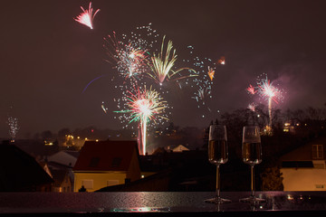 horizontal color picture of two glasses with sparkling wine, in the background blurred fireworks