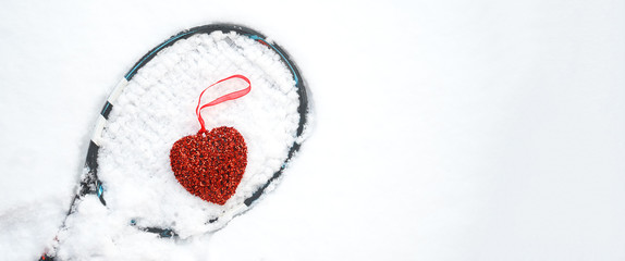 red heart on tennis racket on white snow winter background. I love you tennis player on Valentine's day. concept with tennis play. Flat lay, sport, lifestyle, funny. horizontal, selective focus