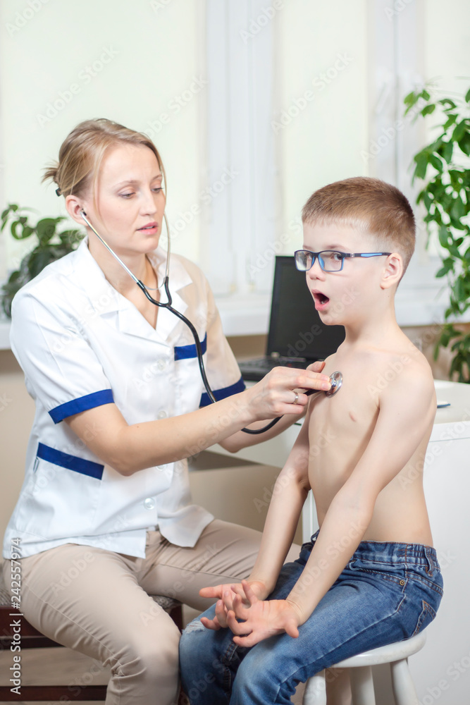 Chłopiec podczas badania stetoskopem przez lekarza pediatrę głęboko oddycha przez otwarte usta. - obrazy, fototapety, plakaty 