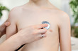 Dłoń lekarki trzyma głowicę stetoskopu przystawioną do piersi dziecka podczas badania. 