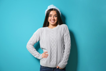 Sticker - Beautiful young woman in warm sweater with hat on color background